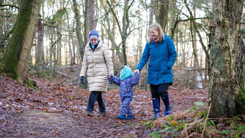 A family with a small child walking in the woodland in winter at Alderley Edge and Cheshire Countryside, Cheshire